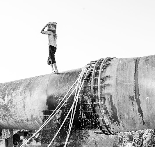 Varied drinking water sources in India - leakages at joints between pipes in the main water pipeline passing across settlements often serve as drinking water source. The leaking water is collected either directly into containers or through plastic pipes inserted into the leakage – Mumbai, Maharashtra